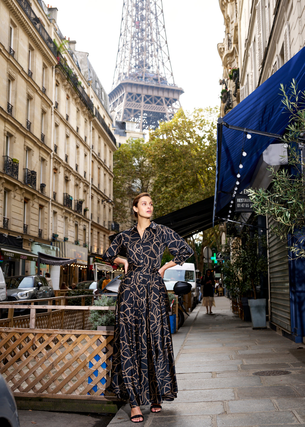 Woman models black and gold maxi dress in front of the Eiffel Tower